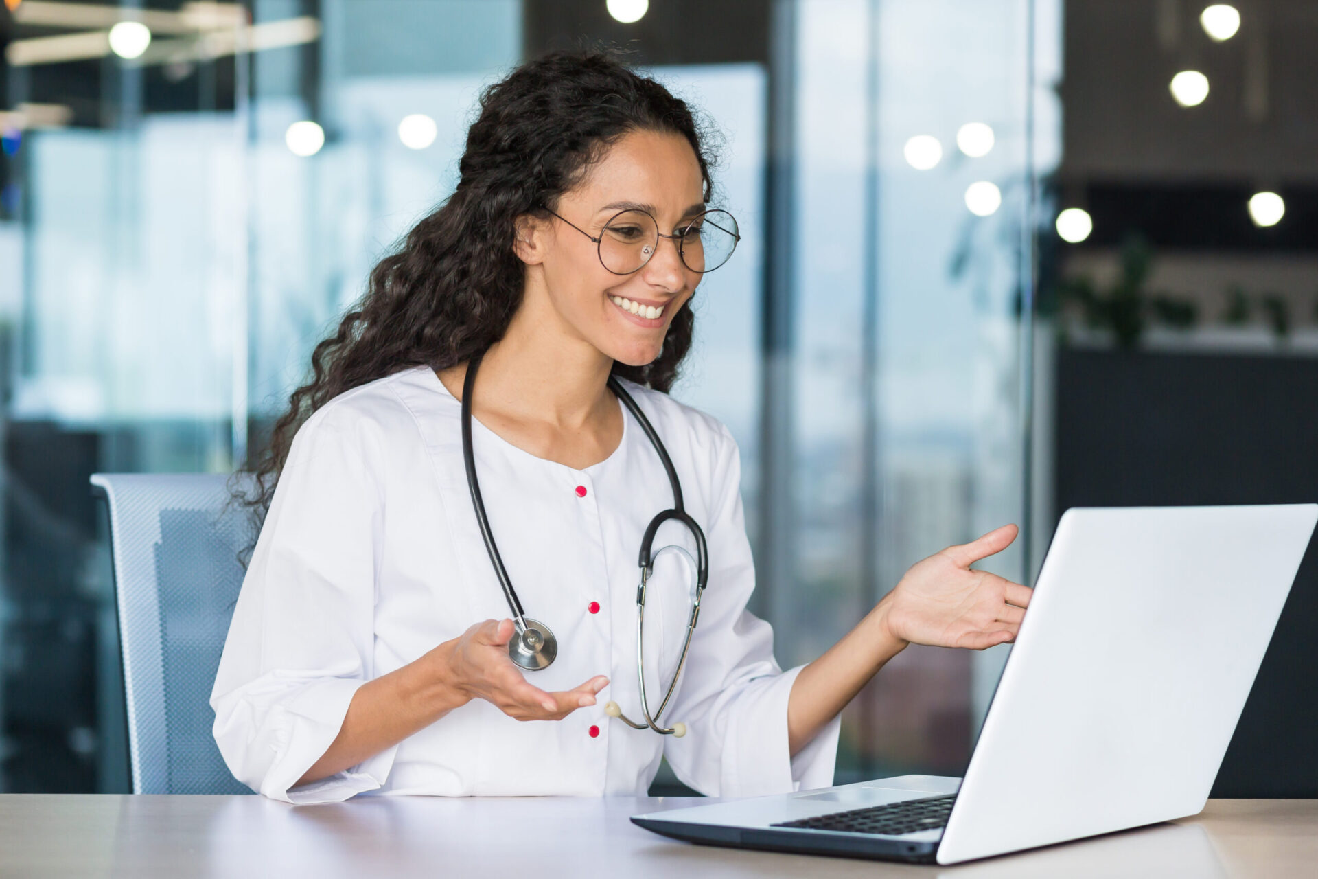 Online consultation of a Latin American doctor with curly hair and glasses, the doctor works inside the office of the clinic, uses a laptop to consult patients remotely